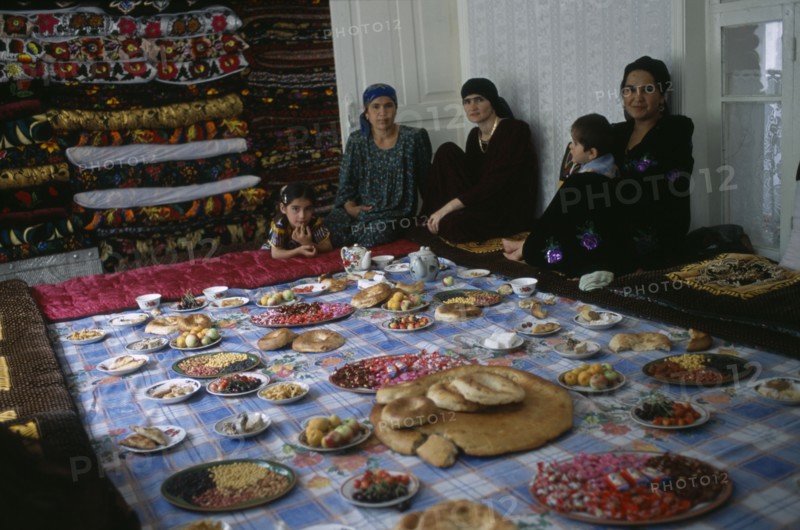 TAJIKISTAN, Food, "Three women and two children sit by a large display of food laid out, awaiting the guests from the village wedding."
