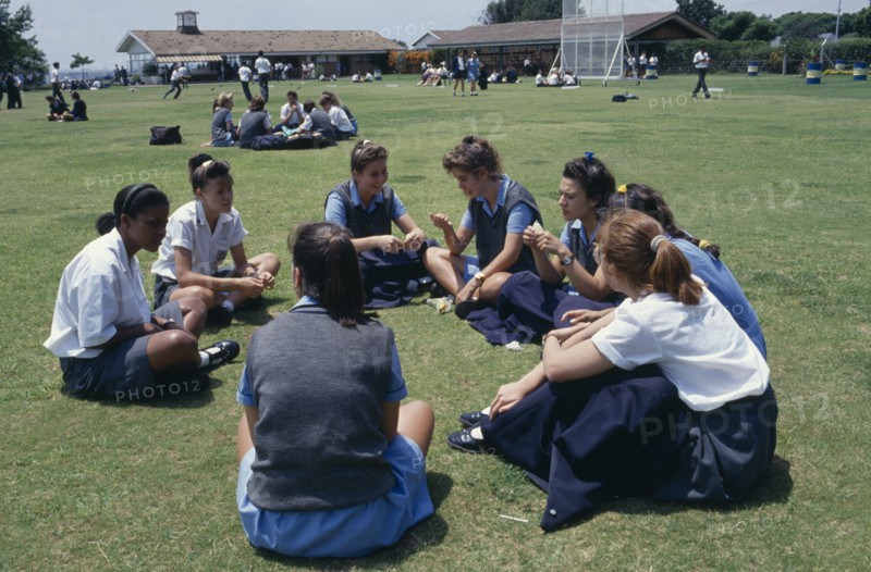 SOUTH AFRICA, Guateng, Johannesburg, Mixed race group of schoolgirls sitting on playing fields during break.