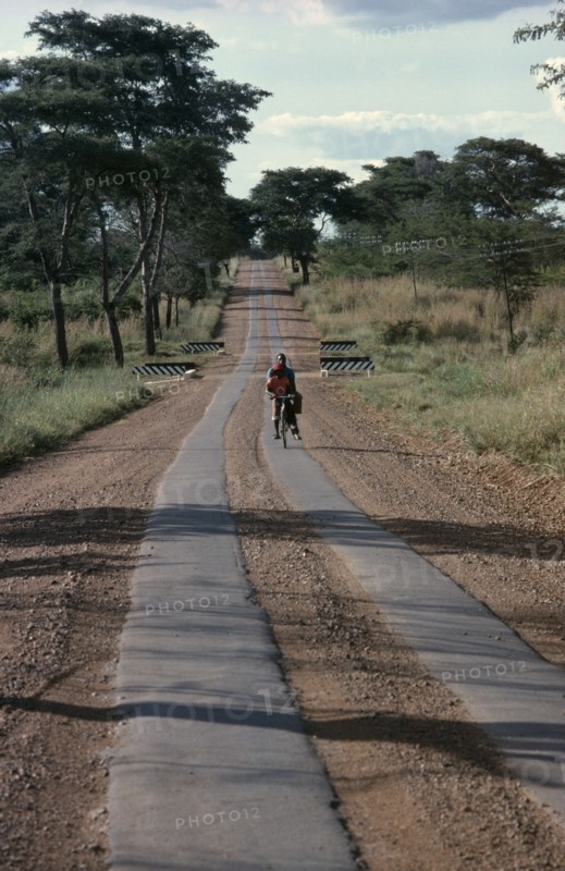 ZIMBABWE, Garooma, Cyclist carrying passenger on the crossbar on strip tar road