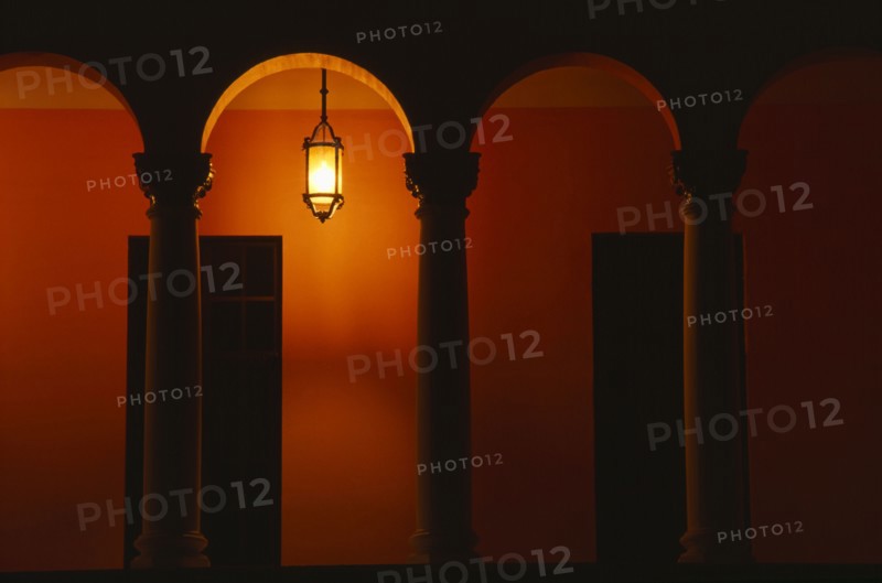 PUERTO RICO, San Juan, Exterior of building at night with pillars and arches and a single light illuminating an orange wall