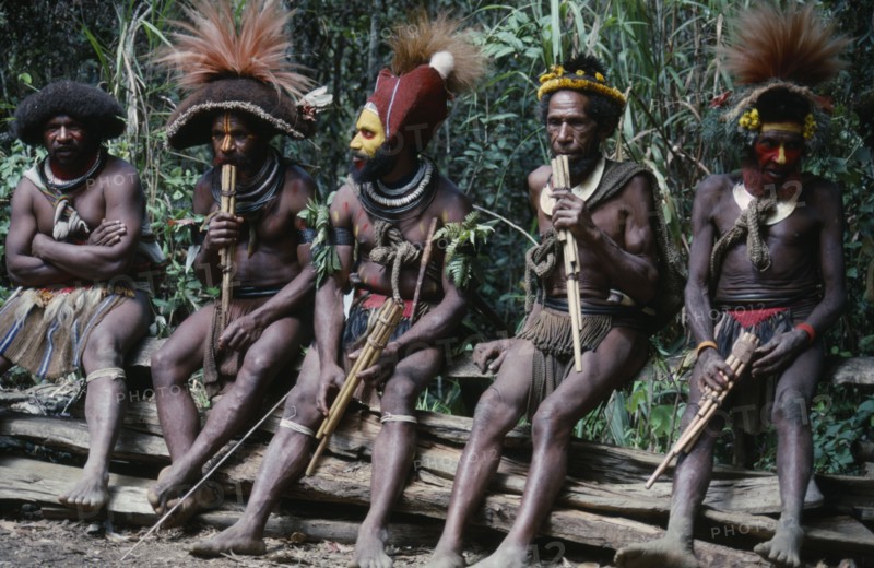 PACIFIC ISLANDS, Melanesia, Papua New Guinea, Southern Highlands. Huli tribe men sat together playing wood instruments at Bachelor Boys centre