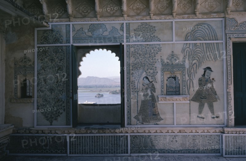 INDIA, Rajasthan, Udaipur, City Palace interior detail with painted walls and arched window framing view over Lake Pichola.