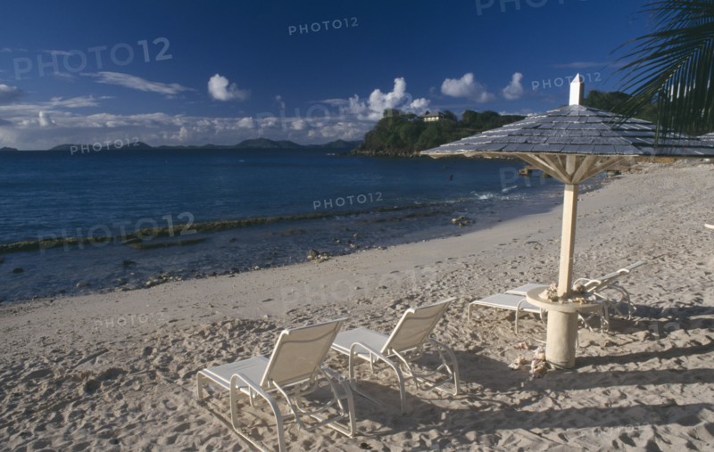 GRENADINES, Mustique, Endeavour Bay. Empty sun loungers on sandy beach with Bequia Island seen from across the sea in the distance