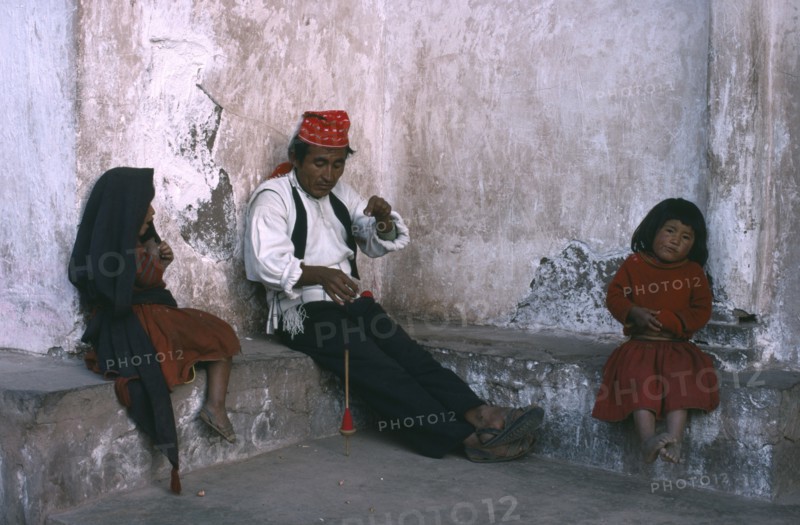 PERU, Puno, Lake Titicaca, Taquile man spinning wool with his two children sitting either side of him.