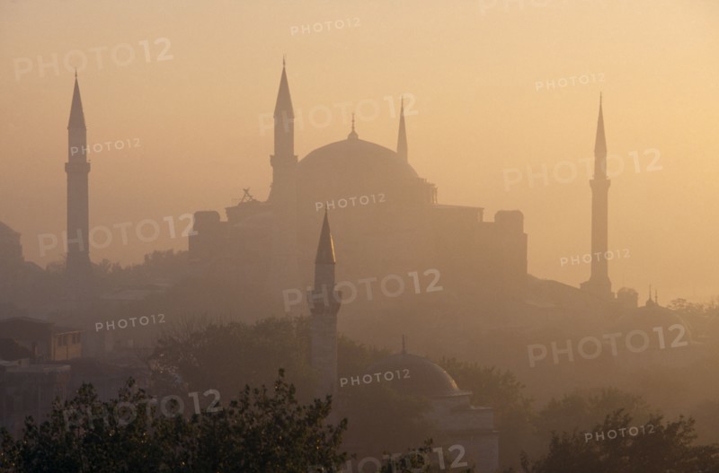 TURKEY, Istanbul, "Dome and minarets of Haghia Sophia silhouetted against hazy, pale orange sky amongst rooftops of the Sultanahmet.  Former mosque now museum."