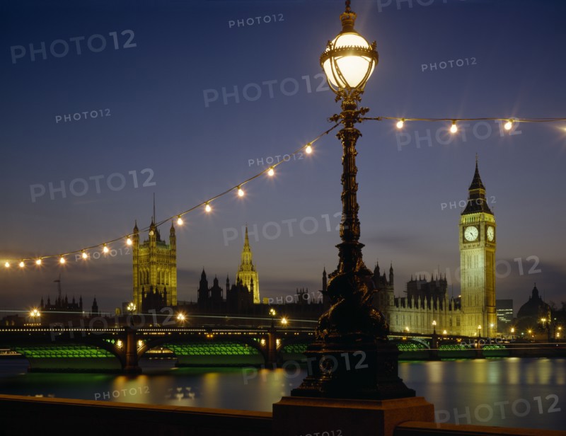 ENGLAND, London, Westminster. Houses of Parliament and Westminster Bridge illuminated at night seen from across the Thames with riverside lighting in the foreground.