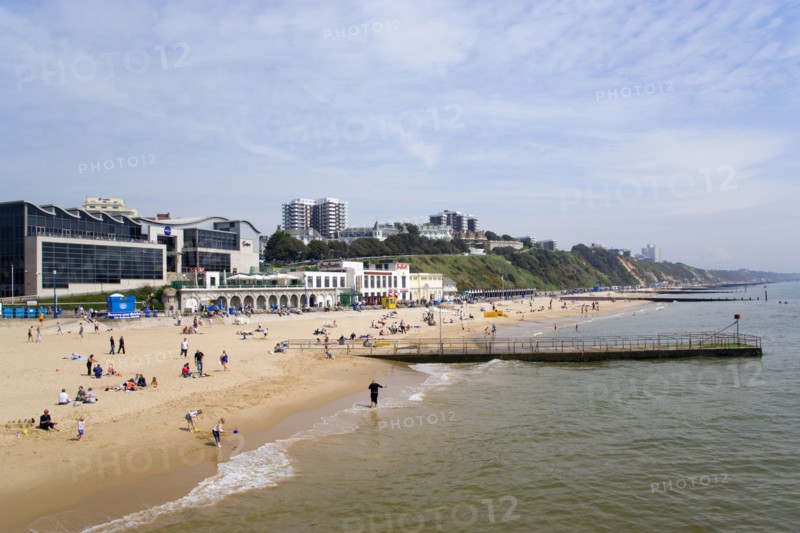 ENGLAND, Dorset, Bournemouth, The East Beach showing the Imax Complex and seafront attractions with people on the beach and at the waters edge between the groynes. Clifftop hotels and flats in the distance