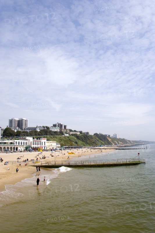 ENGLAND, Dorset, Bournemouth, The East Beach showing the seafront attractions with people on the beach and at the waters edge between the groynes. Clifftop hotels and flats in the distance