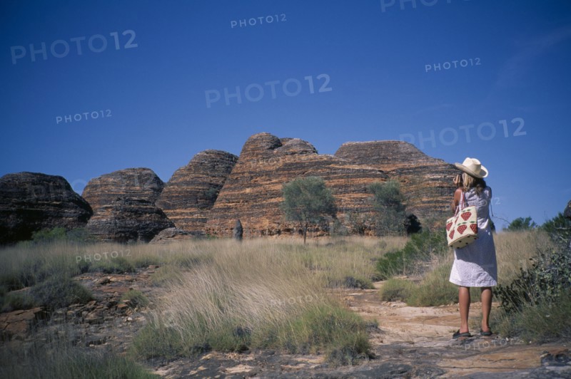 AUSTRALIA, Western ,  Kimberley, Purnululu or Bungle Bungle. Woman wearing straw hat taking picture of striped rock towers