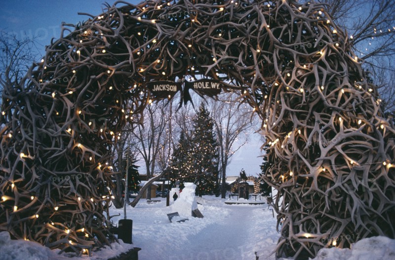 USA, Wyoming, Jackson Town Square. View through Elk Horn Archway decorated with lights towards snow and a Christmas tree.