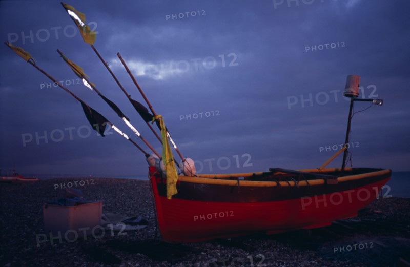 ENGLAND, West Sussex, Worthing, Red and yellow wooden fishing boat pulled up on shingle beach in evening light.