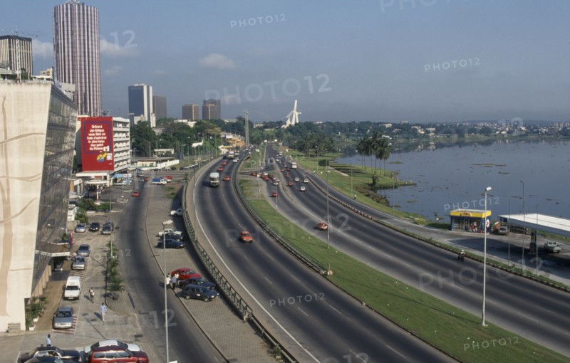 IVORY COAST, Abidjan, "Cityscape with multi lane traffic, skyscrapers and distant view towards modern exterior of St Paul’s Cathedral."