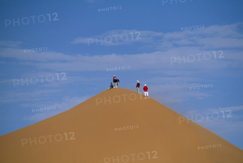 LIBYA, Sahara Desert, Tourists standing on top of Saharan sand dune.