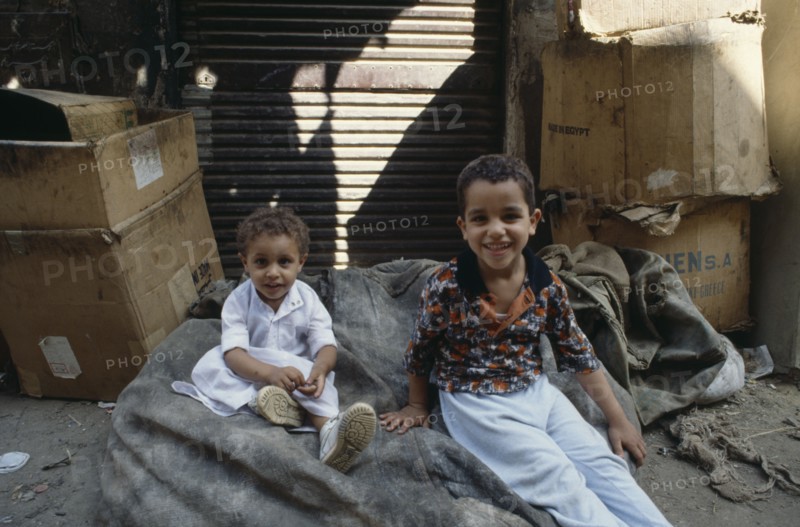 EGYPT, Cairo, Two Street children sat on sacks smiling surrounded by large cardboard boxes