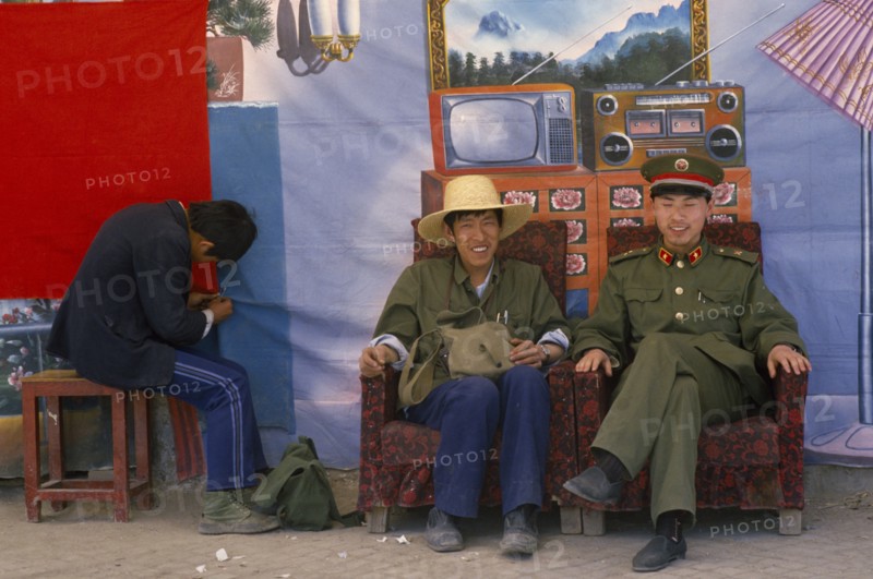 TIBET, Lhasa, "Chinese police pose in front of backdrop featuring desirable electrical goods in domestic interior, equipment they are unlikely to have in reality."