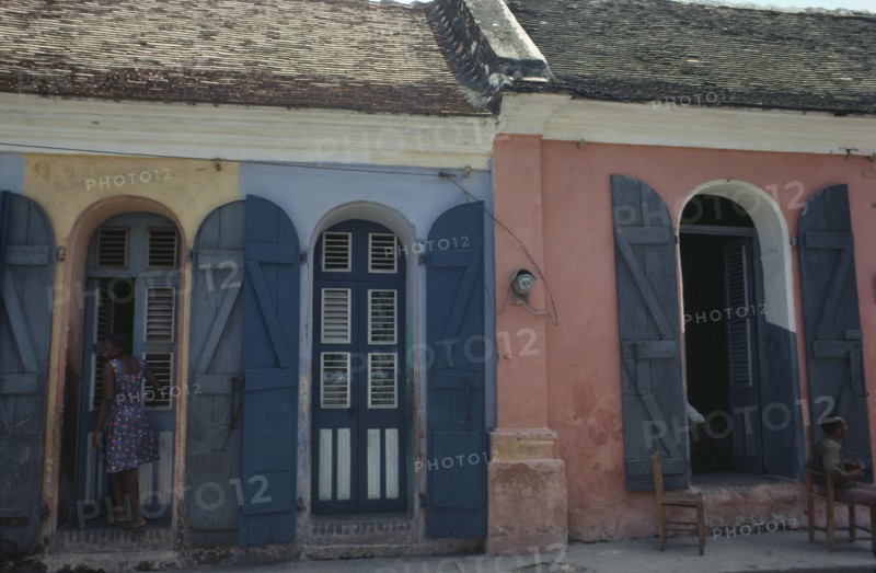 HAITI, Cap Haitien, Street scene with typical colonial style architecture and young woman standing in doorway.