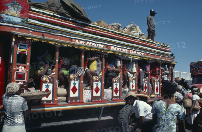 HAITI, Transport, Brightly painted and crowded taptap bus with waiting crowds and food sellers.
