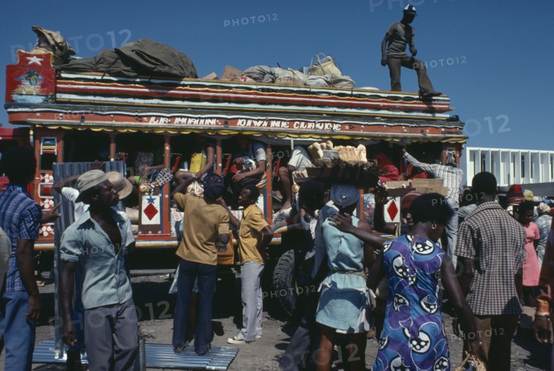 HAITI, Transport, Brightly painted and crowded taptap bus with waiting crowds and food sellers.