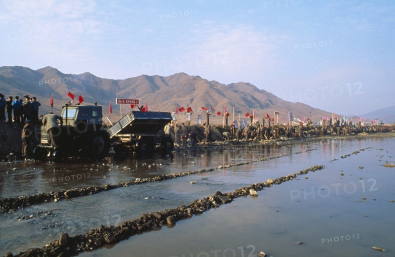 NORTH KOREA, North Hwanghhae Province, Pyongsan County, Juche people in a line reparing flood dykes with red flags fyling and mountains behind them