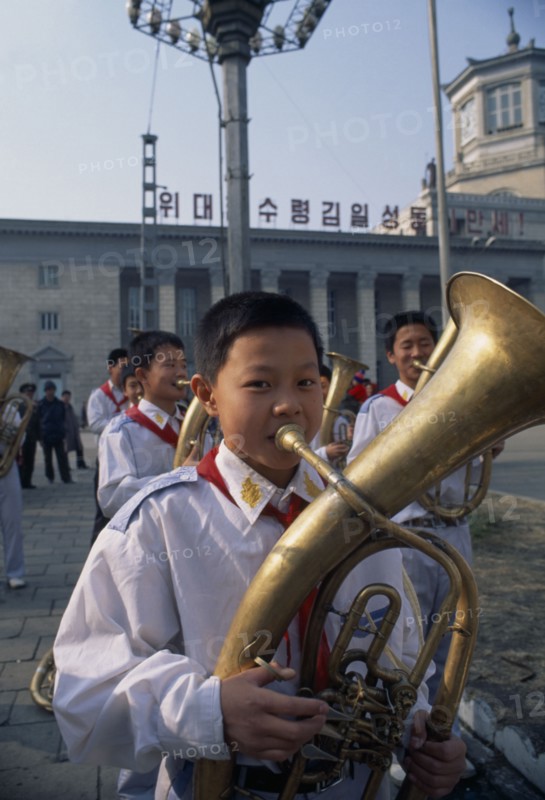 NORTH KOREA, North Hwanghhae Province, Pyongsan County, Boys in Juche band playing brass instruments outside railway station