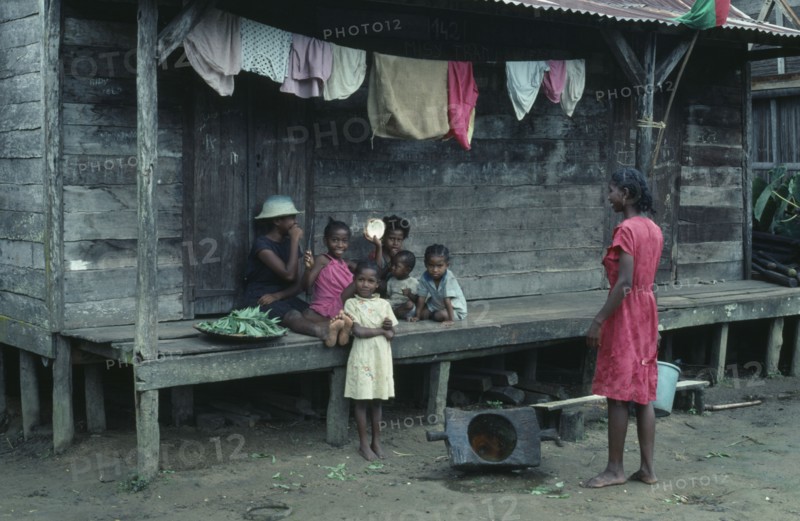 MADAGASCAR, Mananara, Local family sitting on raised wooden veranda of their home with line of washing hanging overhead.