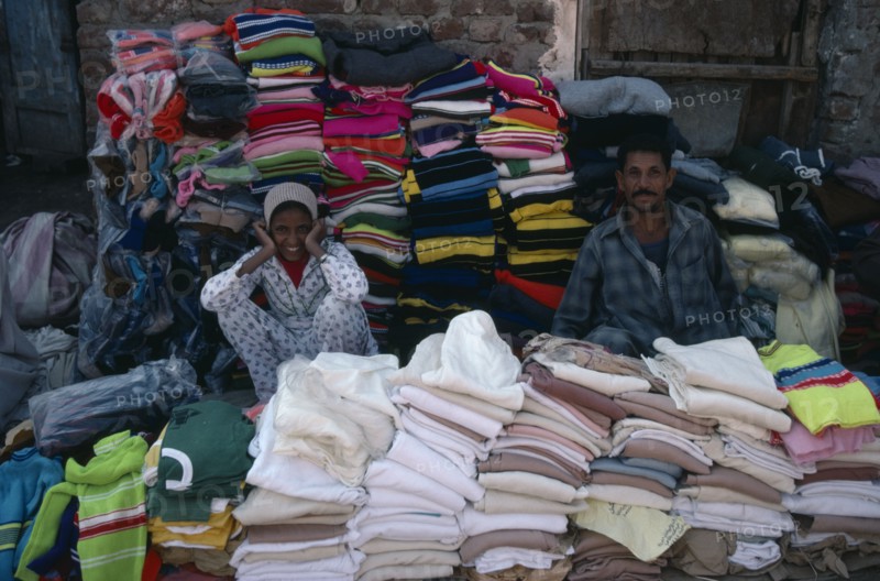 EGYPT, Market, Smiling male and female vendors of pavement stall selling clothing.