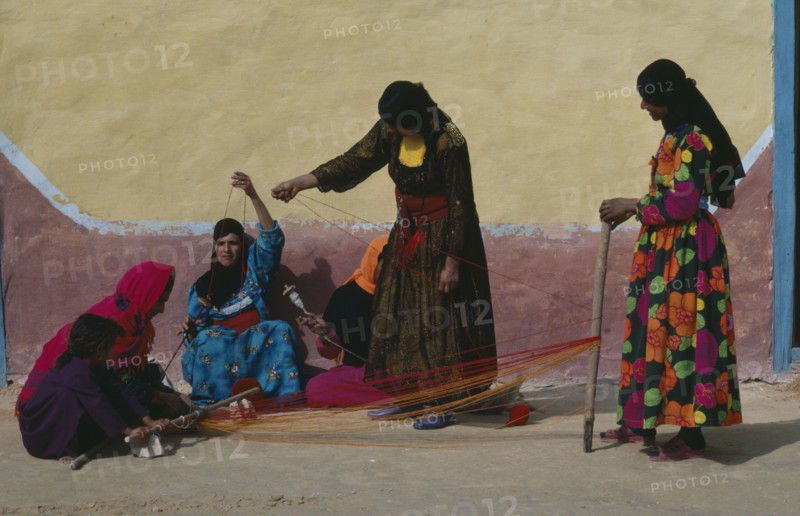EGYPT, Western Desert, Bedouin, Group of Bedouin women in colourful dress weaving and spinning coloured yarn.