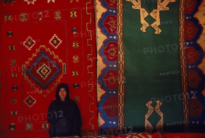 WESTERN SAHARA, SADR, Sahrawi woman standing in front of traditional carpets.