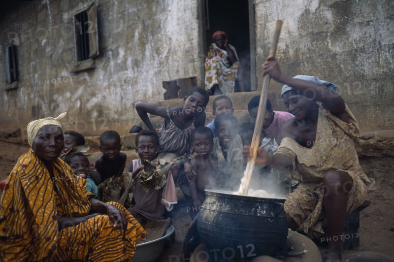 GHANA, Food, Woman in village near Accra stirring cauldron of fufu made from boiled and pounded cassava tubers surrounded by children and other women.