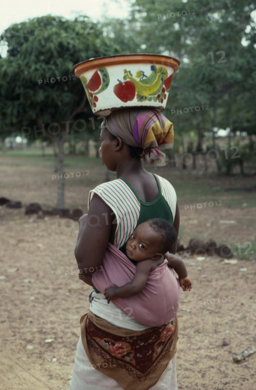 BURKINA FASO, People, Woman carrying baby in sling on her back and painted bowl on her head in area west of Banfora.