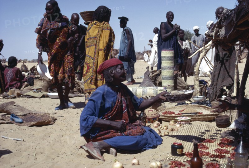 CHAD, Markets, Kanimbo market with woman sat on ground selling foodstuffs with people standing around her