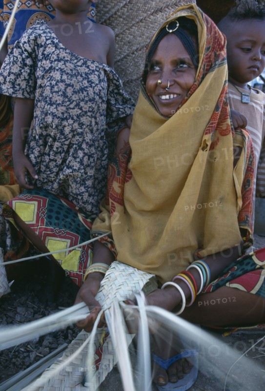 ERITREA, Barentu, Woman making mats with children standing behind her