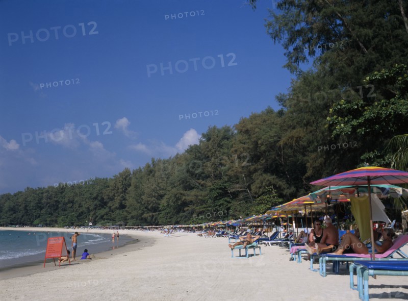 THAILAND, North Phuket, Naiyang Beach, View along the sandy beach with row of sun loungers and colourful parasols. Red sign for boat hire and children playing and digging in the sand.