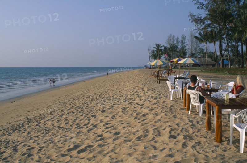 THAILAND, Andaman Sea, Takua Pa district, "Khao Lak, A couple sat at a table on the sandy beach, people walking along the shore and tall palm trees."