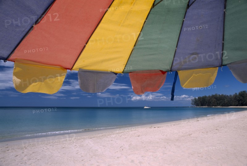 THAILAND, North Phuket, Naiyang Beach, "Close up of a multi coloured parasol on the sandy beach, boat in the distance."