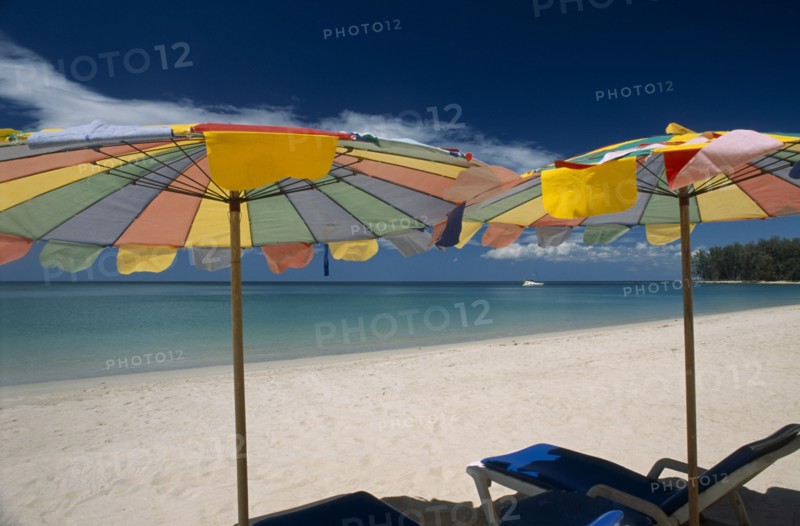 THAILAND, North Phuket, Naiyang Beach, "Two multi coloured parasols and  sun loungers on the sandy beach, boat in the distance."