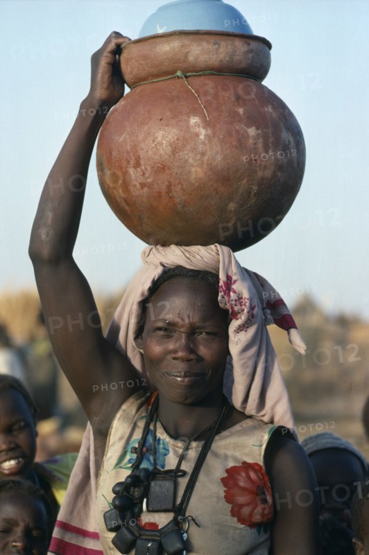 SUDAN, Momei Settlement, Chadian refugee carrying water pot on her head in camp near El Geneina