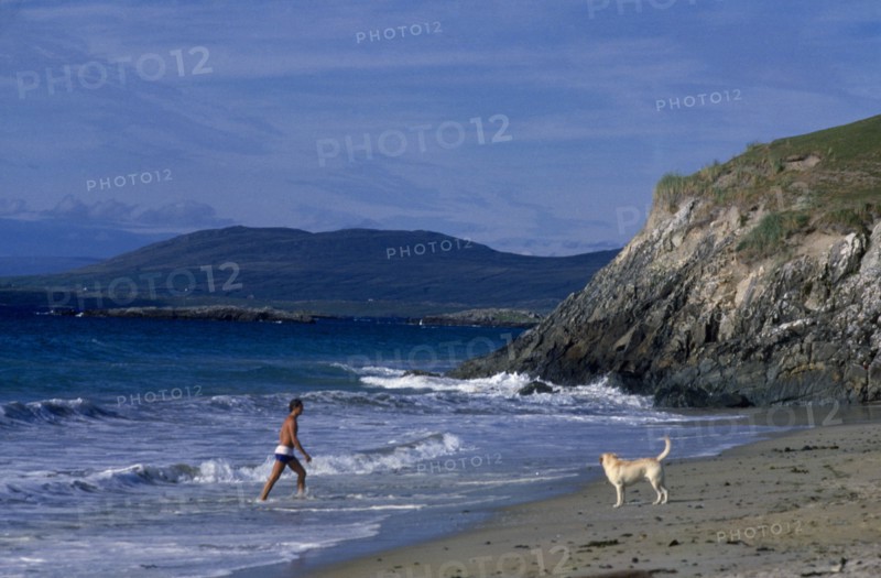 IRELAND, County Galway, Galway, Beach with man walking out of surf towards a dog on the sand