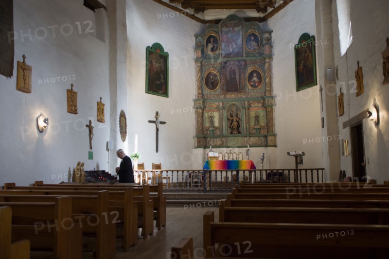 USA, New Mexico, Santa Fe, The altar and nave of the San Miguel Mission church with a priest lighting candles beside the left wall