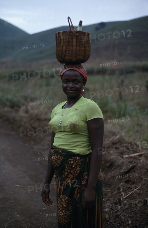 CAMEROON, People, Women, Portrait of young woman carrying woven basket on her head.