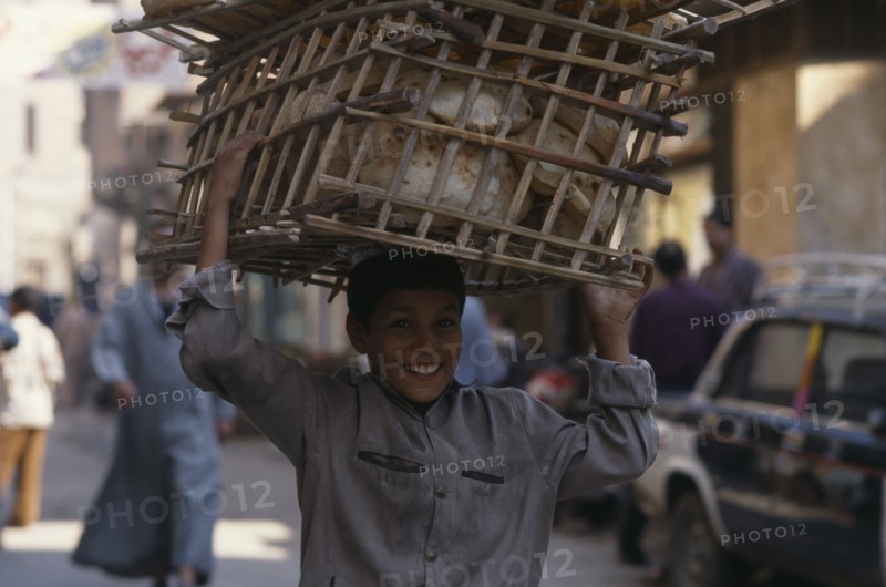 EGYPT, Cairo, Smiling baker’s boy delivering the morning bread carried in basket on his head.
