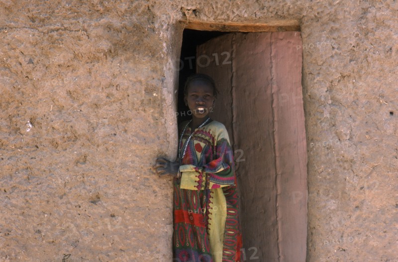 NIGER, Fachi, Young girl looking out of doorway of mud brick building.