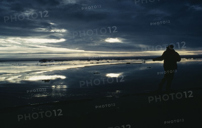 ARCTIC, Landscape, Silhouette of person holding fishing pole with dark sky reflected in the water.