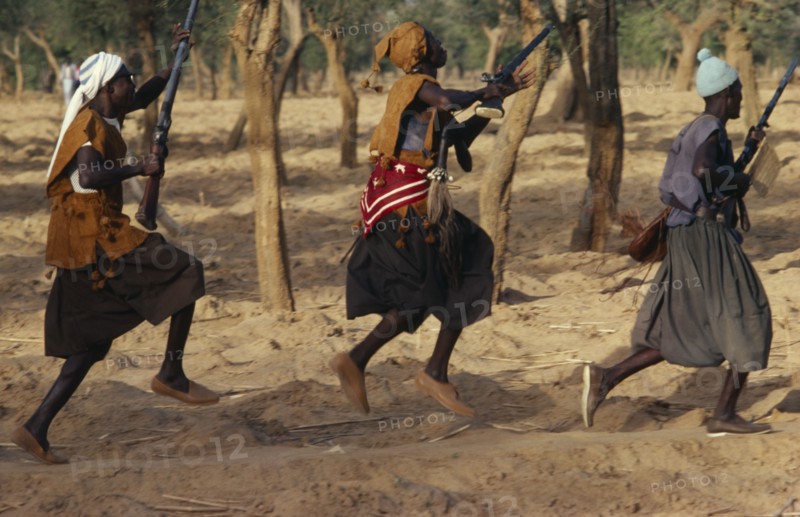 MALI, Ceremony, Dogon funeral dance.  Dancers carrying rifles leaping in line.