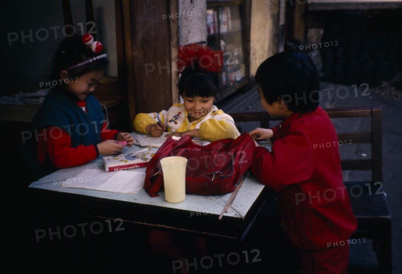 CHINA, Guiyang, Children doing homework outside house.