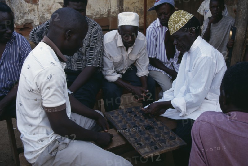 UGANDA, Kampala, Group of men playing board game of mweso in the street.  A type of mancala also known as omweso or mbao using an 8x4 board.