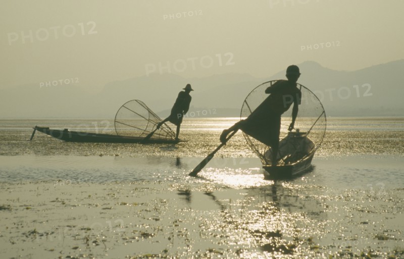MYANMAR, Shan State, Inle Lake, Silhouettes of two Intha fishermen with Sun’s reflection on water.