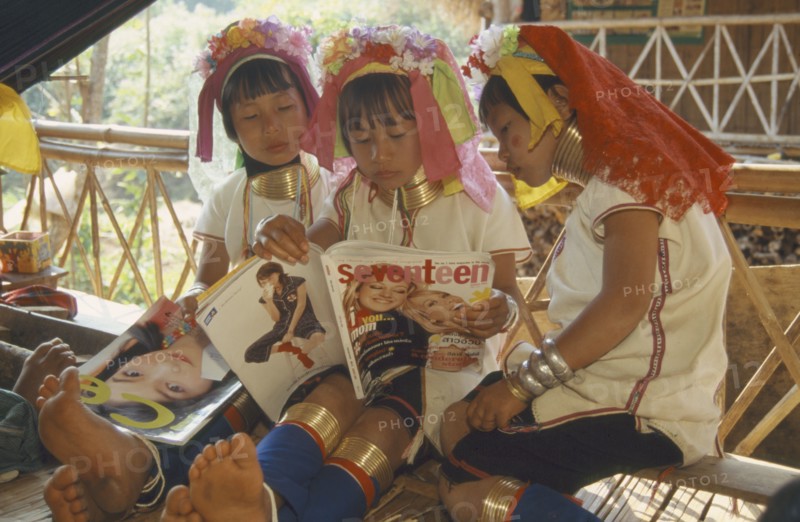 THAILAND, Chiang Rai, "Portrait of young Paduang girls in costume, reading a magazine, long neck, metal rings."