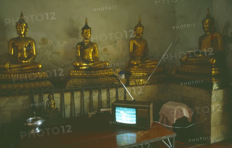THAILAND, Media, Television, Thai boxing on television inside a monastery in front of seated Buddha figures.