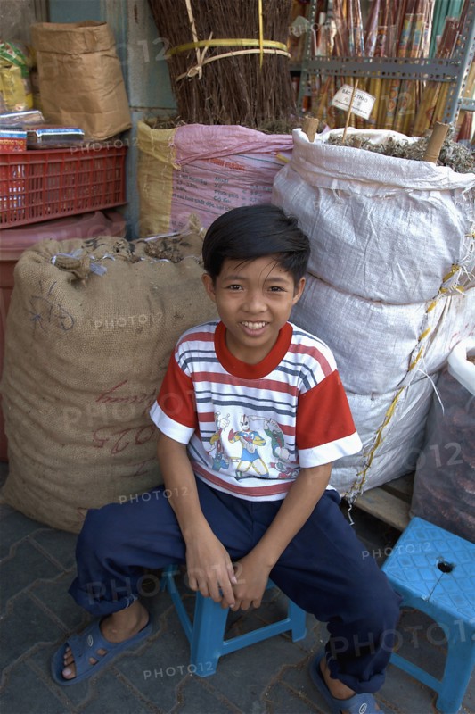VIETNAM, South, Ho Chi Minh City, A young boy sitting next to sacks of dried herbs. Son of the owner of the Chinese herbal shop